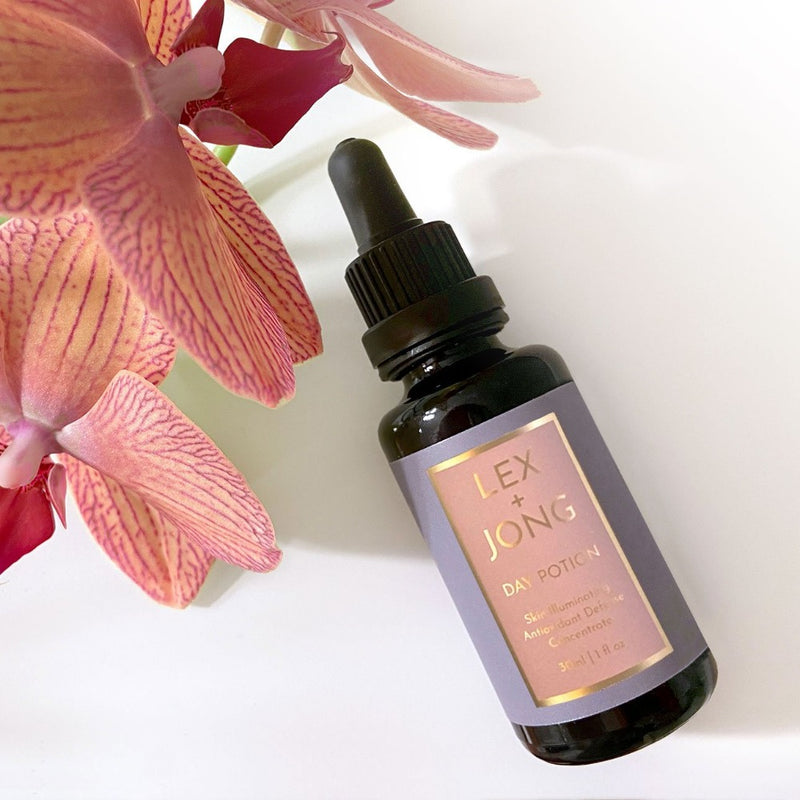 Day Potion (Skin Illuminationg Multi-vitamin Antioxidant Serum Concentrate) bottle - pictured with pink orchid -  helps seven the most ensitive skin thrive